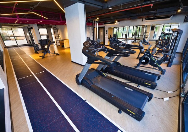 Un gimnasio con cintas de correr, máquinas de pesas y suelo de madera.