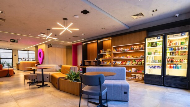 A modern lobby with seating areas, a reception desk, and refrigerated beverage dispensers. - STAY Urbà Home (Goiania)