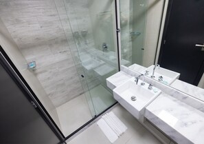 A modern bathroom with a glass shower enclosure, two sinks, and a dark door. - STAY Urbà Home (Goiania)