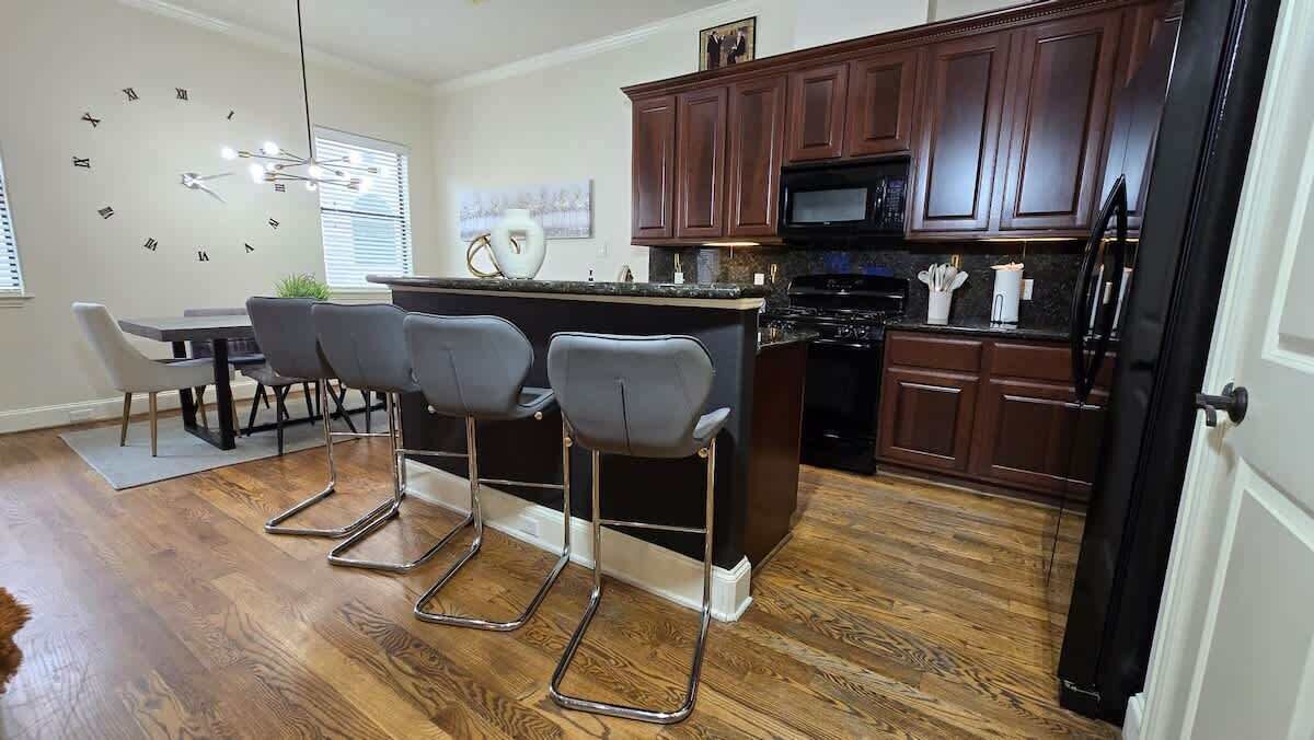 Une cuisine moderne avec des meubles de couleur bois foncé, un îlot central doté de tabourets, un four à micro-ondes et une cuisinière.