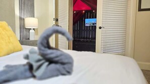 Habitación de hotel con cama, mesita de noche con lámpara y vistas a un balcón con toldo rojo.
