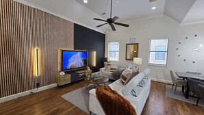 Una sala de estar moderna con un televisor de pantalla plana, un ventilador de techo y un comedor con una mesa y sillas.