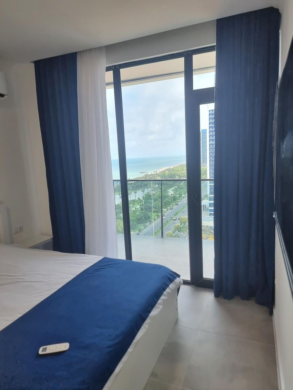 Una habitación de hotel con cama, vistas a la ciudad y un balcón con cortinas.