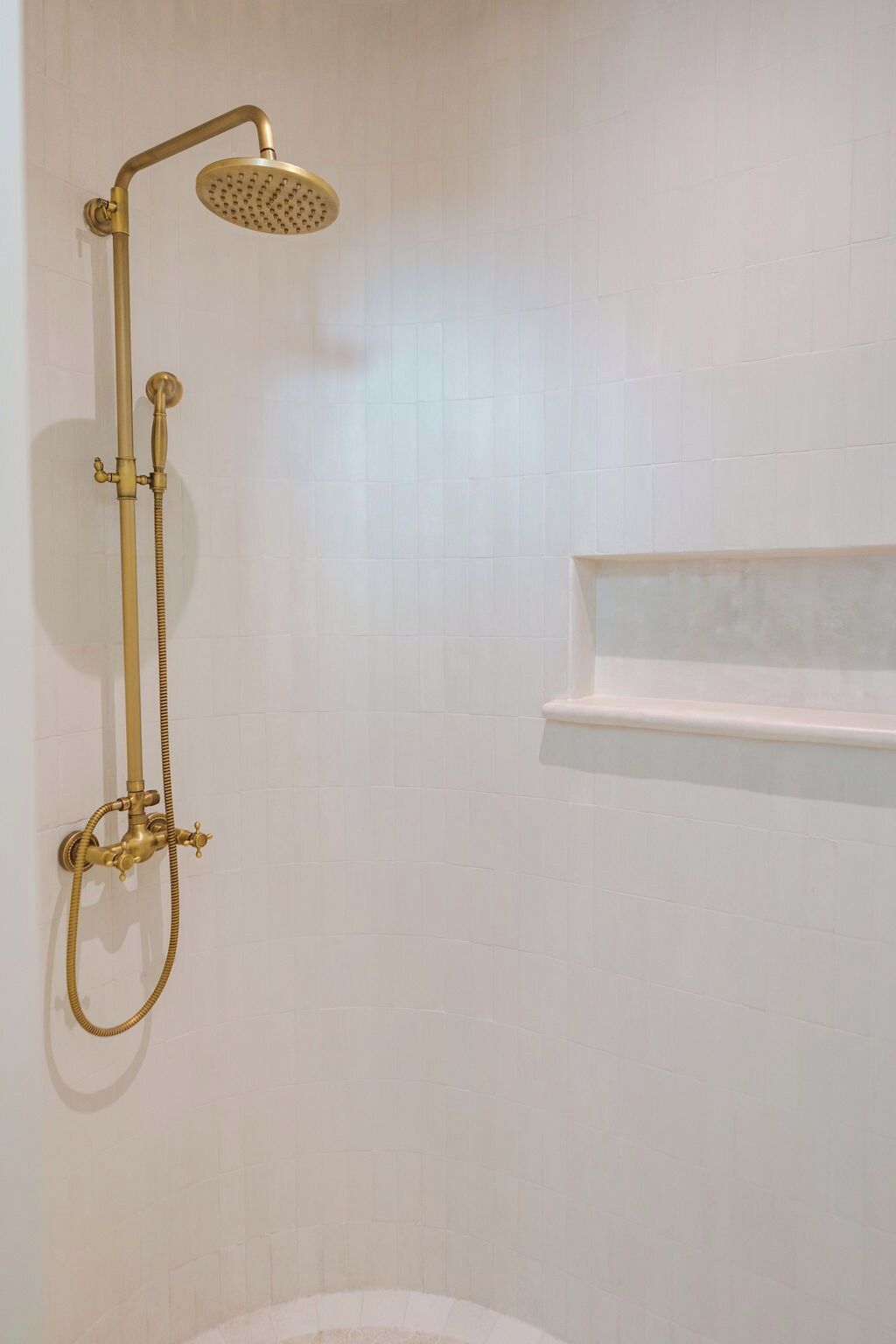 Un bagno con soffione dorato e ripiano a parete.