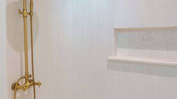 Un bagno con soffione dorato e ripiano a parete.