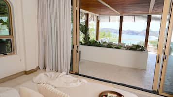 A modern room with a large sliding glass door leading to a balcony with a view of a body of water and mountains.