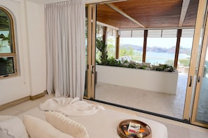 Habitación moderna con un gran ventanal corredero que da a un balcón con vistas al agua y montañas.