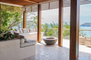 Ein moderner Außenbereich zum Sitzen mit Steinboden, einem weißen Sofa mit Kissen und einer großen Schale.