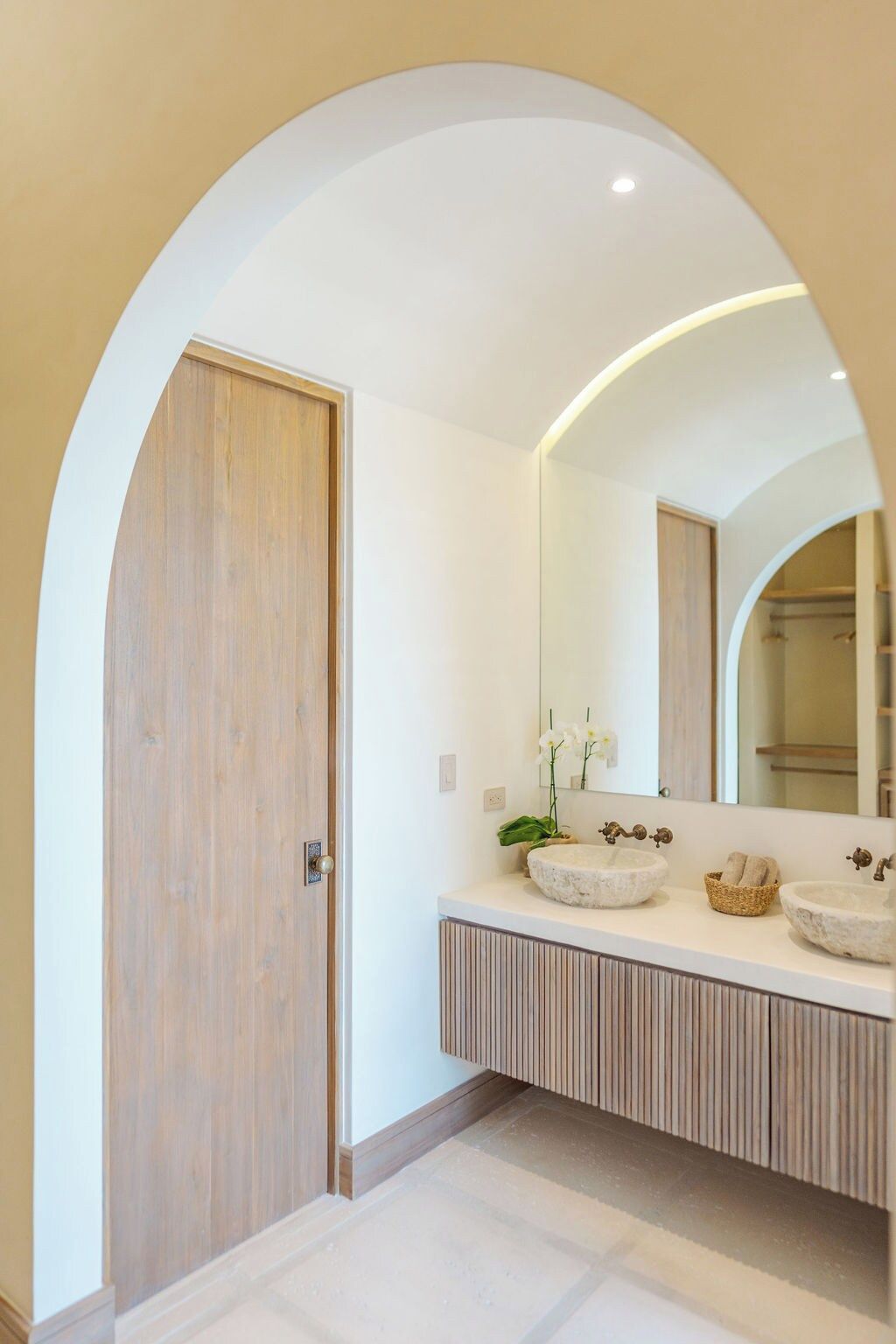Un bagno moderno con una porta in legno, un ampio specchio e due lavabi in pietra.