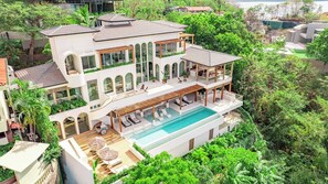 Una casa moderna de varios pisos con piscina, rodeada de exuberante vegetación.