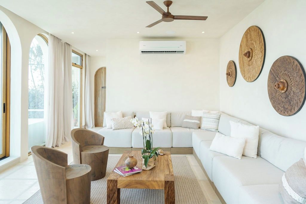 Ein modernes Wohnzimmer mit einer Couch, einem Couchtisch und Sesseln. Ein Deckenventilator und eine Klimaanlage sind ebenfalls vorhanden.