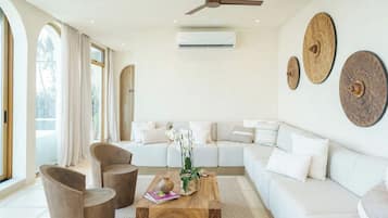 Ein modernes Wohnzimmer mit einer Couch, einem Couchtisch und Sesseln. Ein Deckenventilator und eine Klimaanlage sind ebenfalls vorhanden.