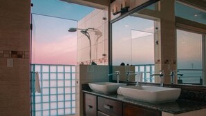 Ein modernes Badezimmer mit einem großen Spiegel, zwei Waschbecken und Blick zum Himmel durch eine Glastür.