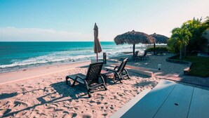Ein Strand mit Liegestühlen und Sonnenschirmen, eine strohgedeckte Konstruktion und Palmen.