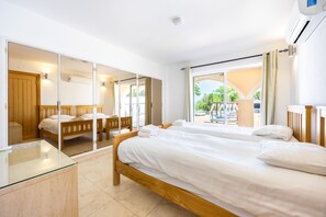 A hotel room with two beds, a glass table, a wooden wardrobe, and a view of the outdoor pool area. - Villa Cristallo - Ten Bedroom Villa, Sleeps 20 (Praia da Luz)