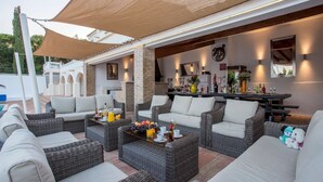 An outdoor patio area with wicker furniture, a bar, and a pool in the background. - Villa Cristallo - Ten Bedroom Villa, Sleeps 20 (Praia da Luz)