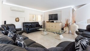 A modern living room with a glass coffee table, leather sofas, a flat-screen TV, and decorative vases. - Villa Cristallo - Ten Bedroom Villa, Sleeps 20 (Praia da Luz)