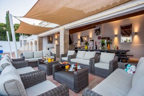 An outdoor seating area with wicker furniture, a bar with various bottles, and a pool in the background. - Villa Cristallo - Ten Bedroom Villa, Sleeps 20 (Praia da Luz)