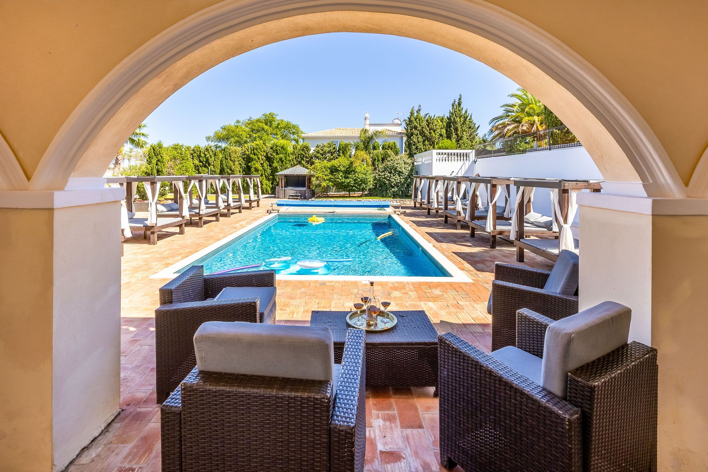 A poolside area with wicker furniture, a pool, and a view of a building in the background.