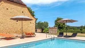 Ein Poolbereich mit Steinmauern, Liegestühlen und Sonnenschirmen.