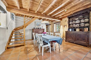 A rustic dining area with a wooden staircase, a stone wall, and a tiled floor.