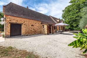 A stone building with a gravel courtyard, a table with chairs, and a large umbrella.