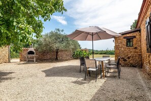 A patio with a table and chairs, a stone oven, and a large umbrella.
