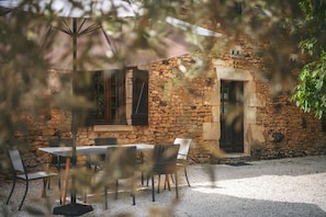 An outdoor seating area with a table and chairs, a stone building with windows and shutters, and a gravel ground. - Robin - Four Bedroom Villa, Sleeps 6 (Sainte-Alvère)