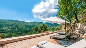 A wooden deck with lounge chairs and an umbrella, overlooking a mountainous landscape.