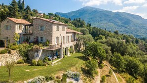 A stone villa with a terrace, surrounded by lush greenery and mountains.