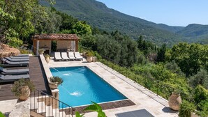 A pool with lounge chairs, a pergola, and a mountainous backdrop.