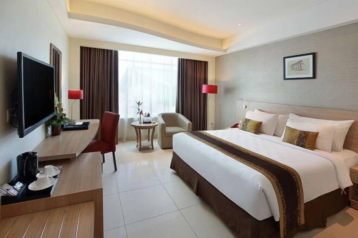 A hotel room with a bed, desk, TV, and a view of the city.