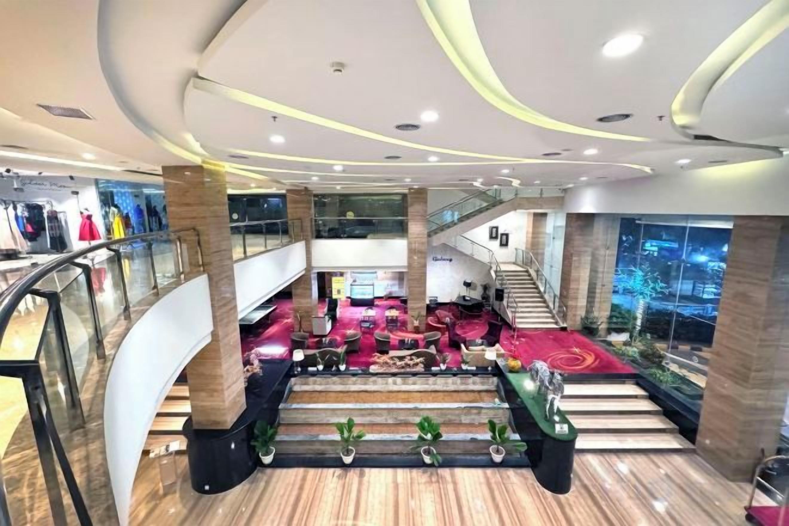 Un interior de varios niveles con una escalera central, escaleras mecánicas y un área de descanso con alfombra roja.