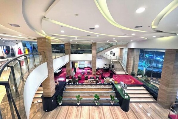 Un interior de varios niveles con una escalera central, escaleras mecánicas y un área de descanso con alfombra roja.