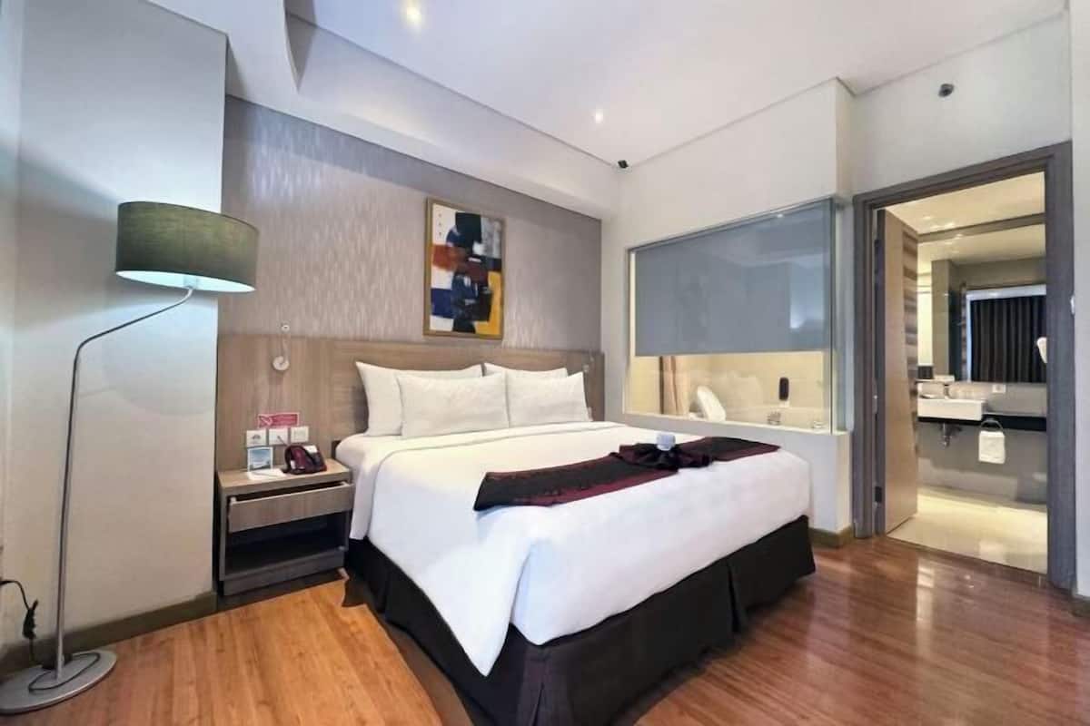 A modern hotel room with a large bed, bedside table, lamp, and a view of the bathroom.