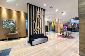 A hotel lobby with a black sofa, a round table with a pink table runner, and a decorative wall panel. - Galaxy Hotel Banjarmasin (Banjarmasin)