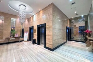 Un hall de hotel con suelo de mármol, una recepción, ascensores y una araña.
