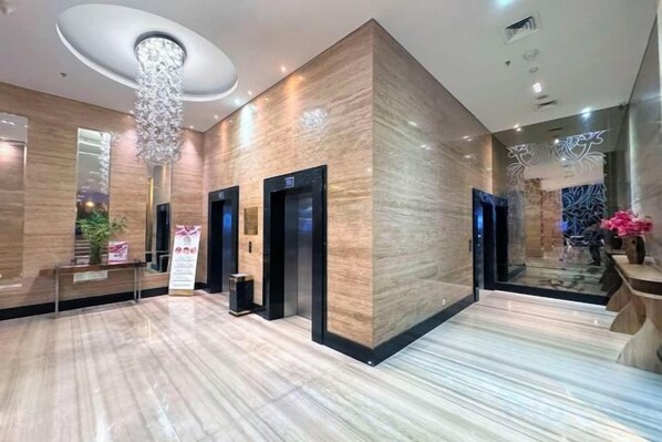 Un hall de hotel con suelo de mármol, una recepción, ascensores y una araña.