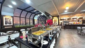 A buffet setup with multiple serving stations, a bar area, and a view through a large window.
