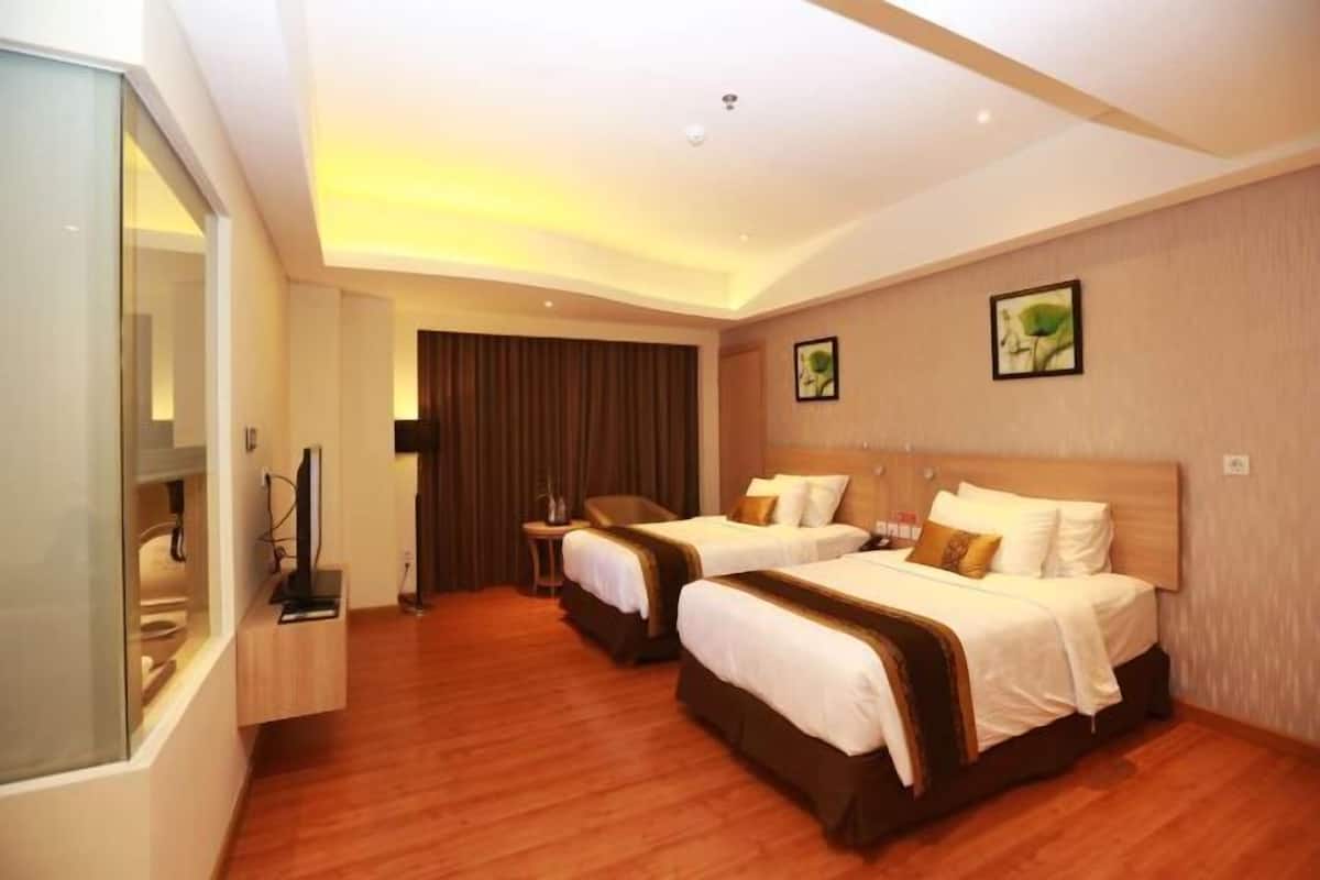 A hotel room with two beds, a TV, a desk, and a mirror.