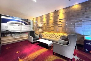 Un moderno vestíbulo de hotel con un sofá, sillones, una mesa de centro y una alfombra roja con motivos de estrellas.