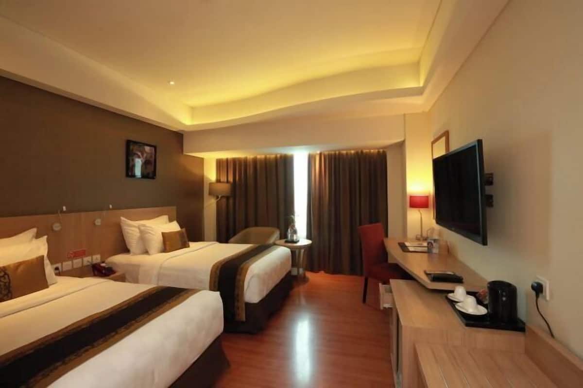 A hotel room with two beds, a desk, a TV, and a window with curtains.