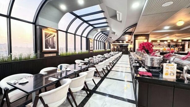 Un ristorante moderno con un lungo bancone, sedie bianche e vista sulla città attraverso ampie finestre.