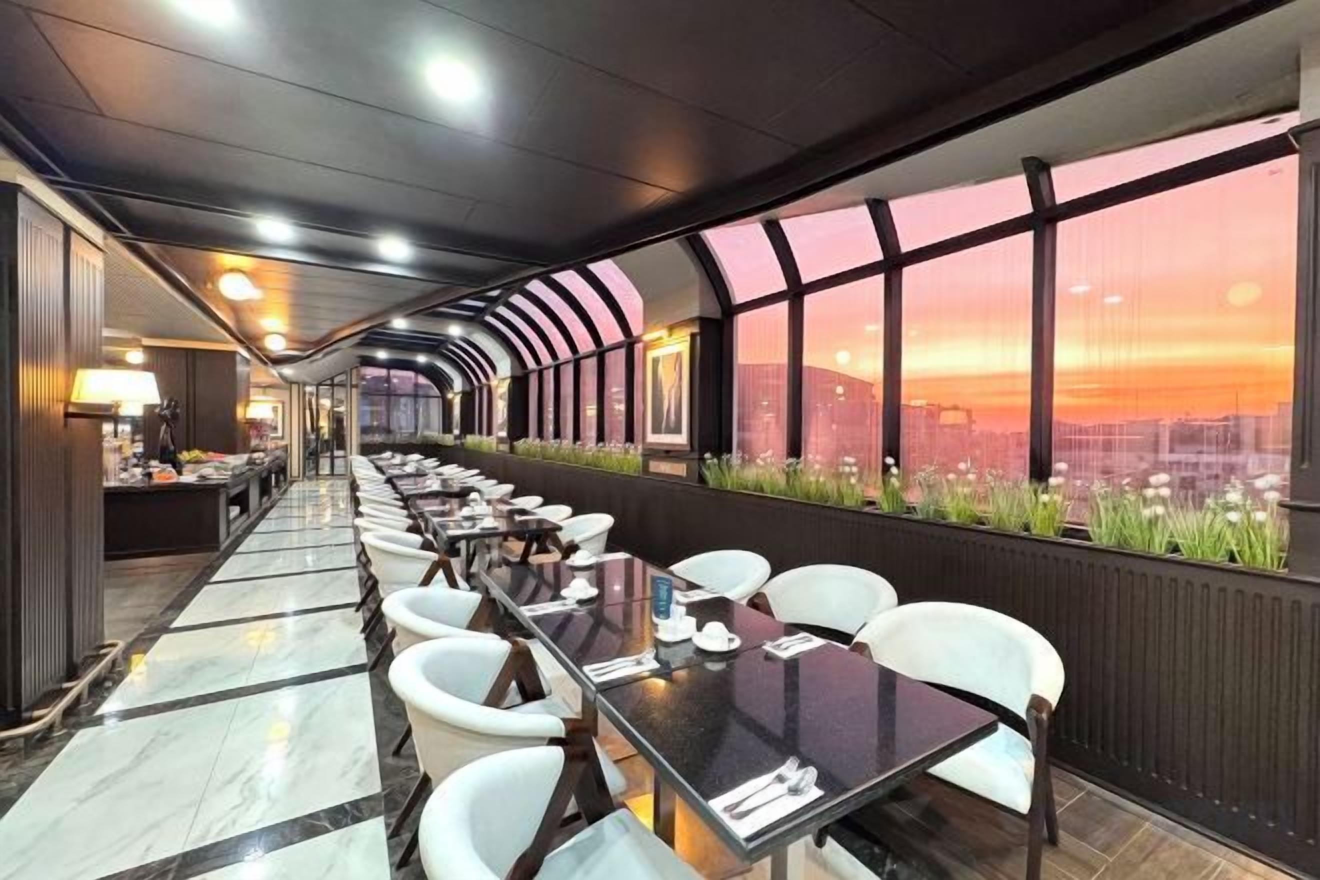 Un'ampia sala da pranzo con tavoli e sedie, grandi finestre vista città e un design d'interni moderno.