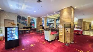 A hotel lobby with a red carpet, a reception desk, and a staircase in the background.