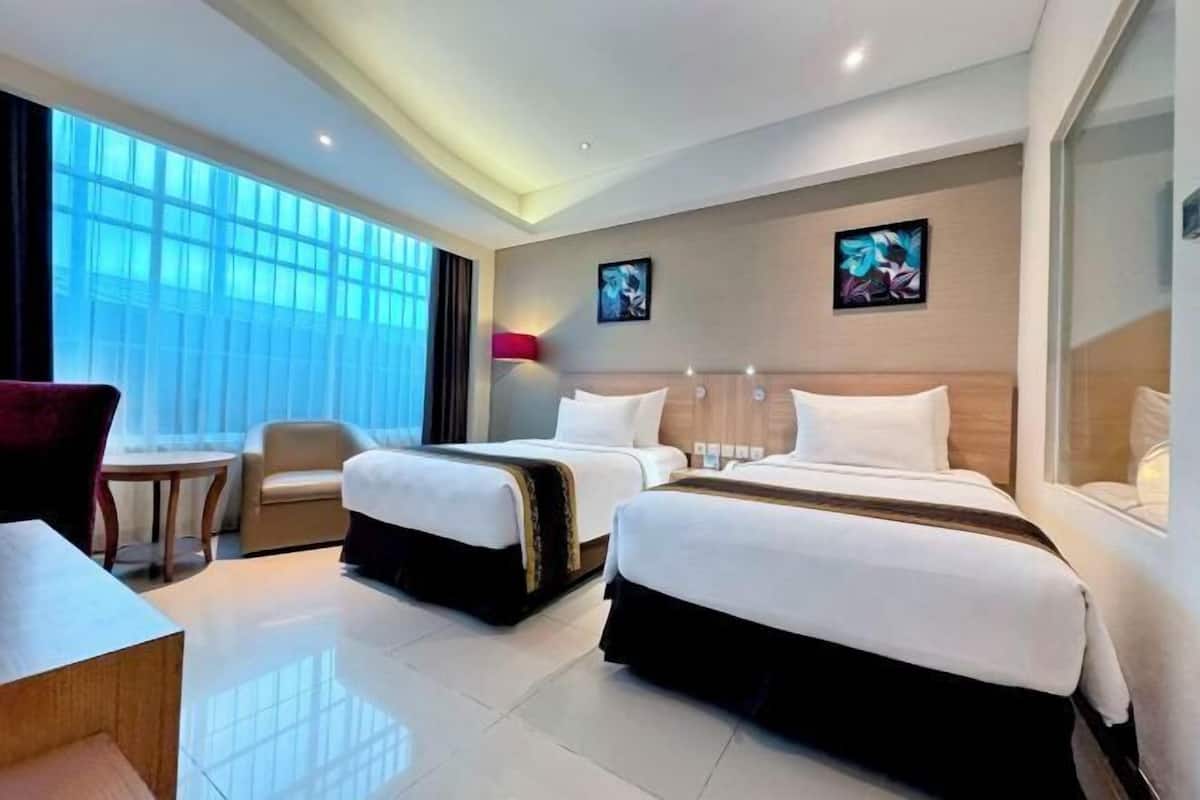 A hotel room with two beds, a desk, a chair, and artwork on the walls.