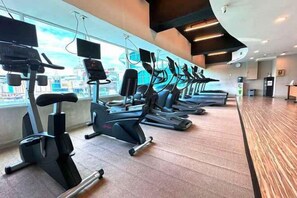 Un gimnasio con varias máquinas de cardio, un ventanal con vista a la ciudad y suelo de madera.