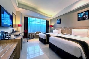 Habitación de hotel con escritorio, dos camas, televisor y obras de arte en las paredes.