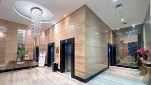 Una hall moderna con pavimento in marmo, pannelli in legno e un lampadario centrale.