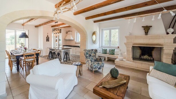 Amplia sala de estar con chimenea, vigas de madera y un comedor con mesa dispuesta para seis comensales.